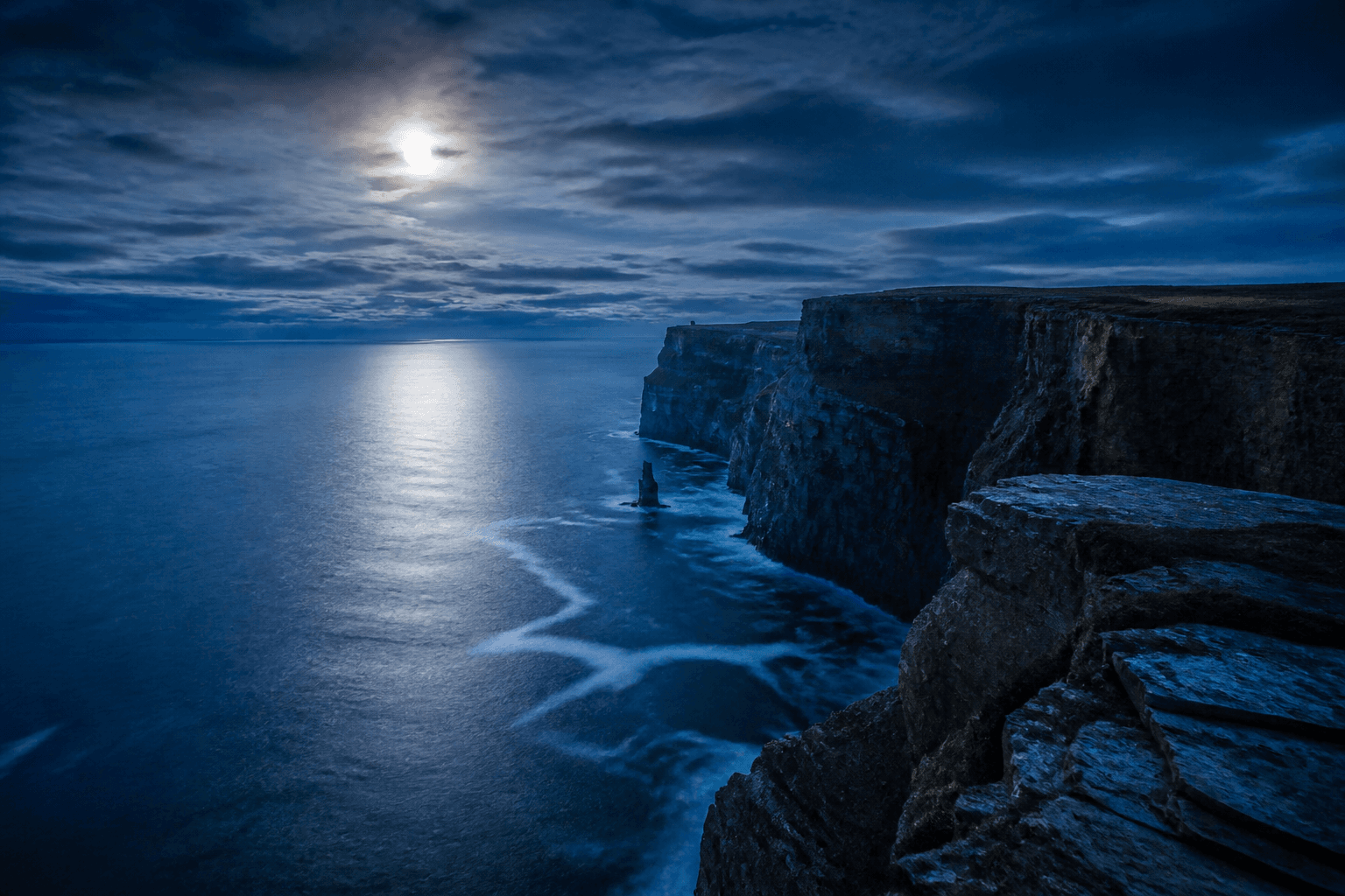 Falaises côtières à l’heure bleue, mer argentée sous la lune.